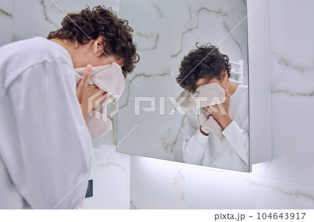 Young guy in bathroom near mirror washing face, wiping with towel 104643917