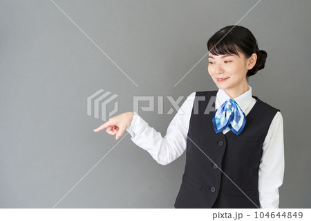指で指し示すベストにリボンタイの制服を着た受付業務、事務業務の女性 104644849