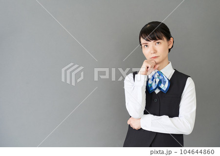 考える仕草をする、ベストにリボンタイの制服を着た受付業務、事務業務の女性 考える仕草をする、ベストにリボンタイの制服を着た受付業務、事務業務の女性 104644860