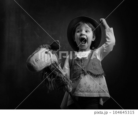 Cute little girl dressed like a cowboy playing with a homemade horse. Cute little girl dressed like a cowboy playing with a homemade horse. 104645315