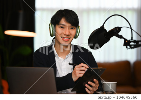 Asian man podcasters using laptop and condenser microphone to recording podcast in small home studio 104645360