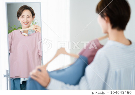 鏡の前で服選びをしている若い女性　ファッションイメージ 104645460