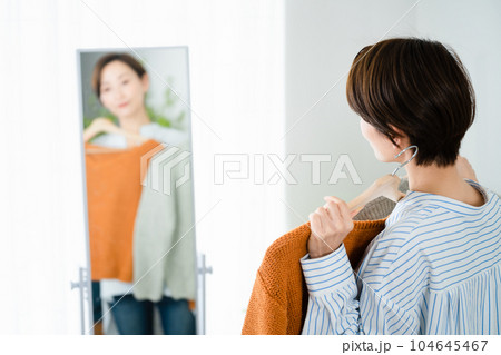 鏡の前で服選びをしている若い女性　ファッションイメージ 104645467