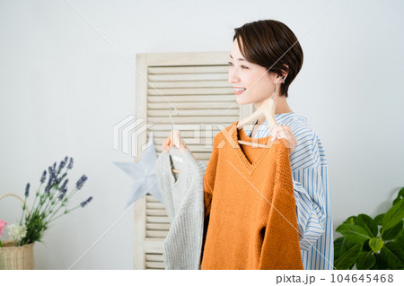 鏡の前で服選びをしている若い女性　ファッションイメージ	 104645468