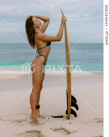 Surfer girl with surfboard on beach goes to surfing. Woman in sexy bikini standing with surf 104645906
