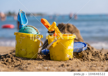 Children's beach toys - buckets, spade and shovel on sand on a sunny day. Bright toys on the background of the sea. Children's beach toys - buckets, spade and shovel on sand on a sunny day. Bright toys on the background of the sea. 104646522
