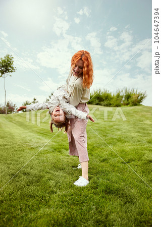 Joyful weekends. Beautiful redhead young woman, mother playing with her little daughter in the park on warm summer day 104647394
