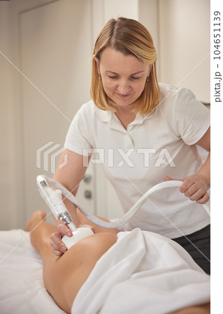 lymphatic drainage, reduce cellulite, anti cellulite massage. Young woman from beauty salon performs beauty services, body shaping, masseurs perform vacuum roller massages for clients, figure 104651139