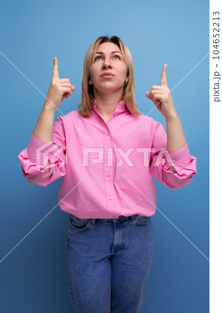 young blond caucasian woman with flowing straight hair dressed in a pink blouse and jeans pointing 104652213