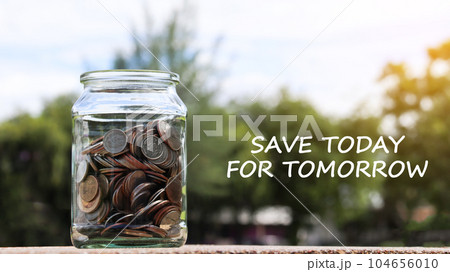 Coins in glass jar with the text save to day for tomorrow with blurred green trees background, concept of money savings                               104656010