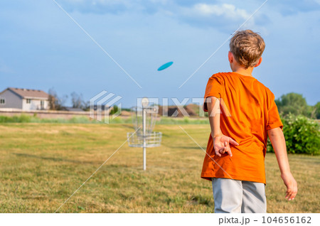 Young Caucasian male boy aiming a disc golf at a chain goal.  Young Caucasian male boy aiming a disc golf at a chain goal.  104656162