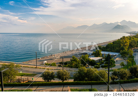 Aerial view of scenic and popular Konyaalti beach in Antalya resort town. Majestic mountains with sunset haze in the background. Vacation and holiday in Turkey 104658320