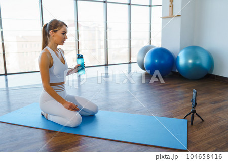 Young Woman on Yoga Mat Filming Online Workout with Phone Young Woman on Yoga Mat Filming Online Workout with Phone 104658416