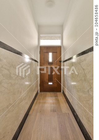 a long hallway with marble walls and wood flooring on either side of the room, there is an open door a long hallway with marble walls and wood flooring on either side of the room, there is an open door 104658486
