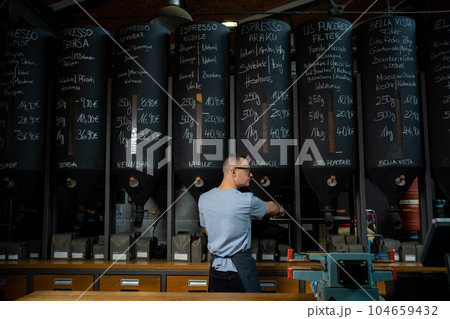 Barista roasting shop worker standing at counter pouring coffee beans. 104659432