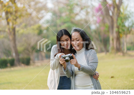 Asian teenage mother and daughter walking in park with camera to capture memories. 104659625