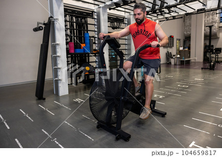 Adult athletic man doing cycling on exercise bikes at the gym. Adult athletic man doing cycling on exercise bikes at the gym. 104659817