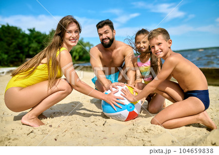 Mother father son and daughter playing inflatable ball on sand by river in summer. Mother father son and daughter playing inflatable ball on sand by river in summer. 104659838