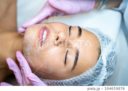 Unrecognizable female cosmetologist apply mask on woman's face, spa procedures, cleansing face. 104659876