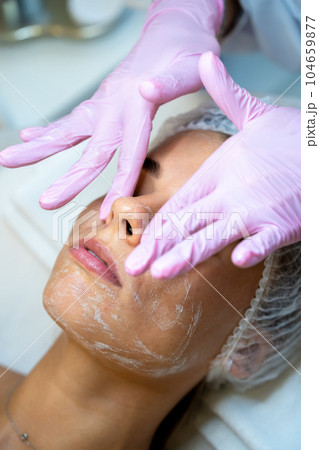 Woman cosmetologist apply cream on female's face, doing beauty procedures. 104659877