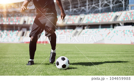 African American man playing football on the stadium field. A man runs with a soccer ball across the field. 104659988