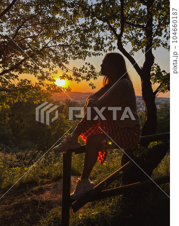 A woman sits on a fence overlooking the city and the sunset 104660187