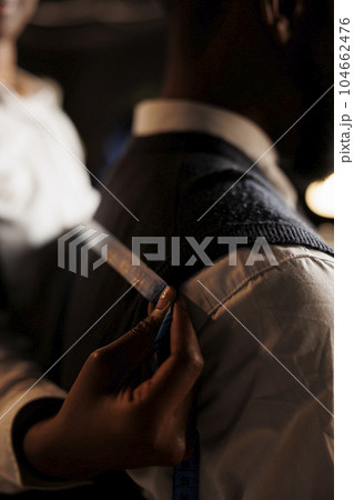 Extreme close up of meticulous skilled tailor taking sartorial stylish garment measurements on client. Seamstress manufacturing custom made refined premium quality business suit in atelier shop 104662476
