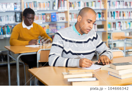 Focused adult latin american student studying in library 104666342