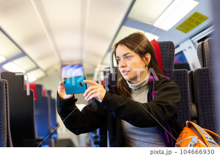 Interested female traveler filming landscapes behind glass in express train Interested female traveler filming landscapes behind glass in express train 104666930