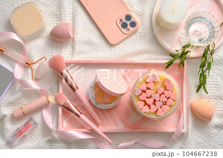 Lovely pink concept with a rectangle tray featured scented candle, cushion compact, makeup brushes and other makeup stuffs displayed. Makeup products mockup 104667238