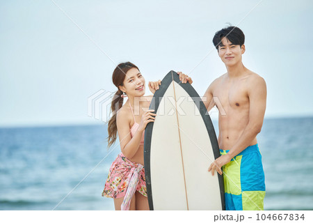 couple holding surfboards at beach 104667834