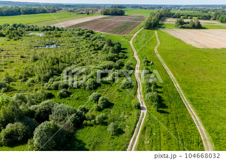 A view from a height of a country road receding into the distance running between green fields A view from a height of a country road receding into the distance running between green fields 104668032