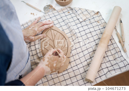 woman creates pattern on a leaf shaped piece of clay by hands in artistic studio woman creates pattern on a leaf shaped piece of clay by hands in artistic studio 104671273