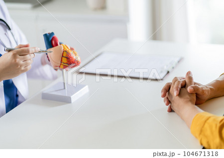 Cardiology Consultation treatment of heart disease. Doctor cardiologist while consultation showing anatomical model of human heart with aged patient talking about heart diseases. 104671318