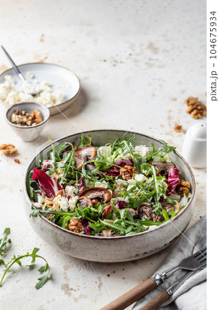 Green salad with feta cheese, arugula, mushrooms, walnut in ceramic bowl on textured background. Healthy summer lunch or dinner Green salad with feta cheese, arugula, mushrooms, walnut in ceramic bowl on textured background. Healthy summer lunch or dinner 104675934