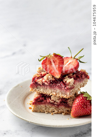Two pieces of Strawberry granola bars on a pate on white marble background close up. Delisious homemade oat squares for breakfast with copy space Two pieces of Strawberry granola bars on a pate on white marble background close up. Delisious homemade oat squares for breakfast with copy space 104675959