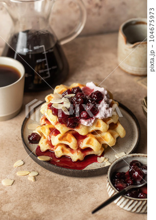 Belgian waffles with sour cream, cherry jam and almond petals topping and coffee on beige kitchen background. Sweet morning breakfast 104675973
