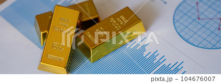 Small gold ingots on financial statistics document with charts and graphs Small gold ingots on financial statistics document with charts and graphs 104676007