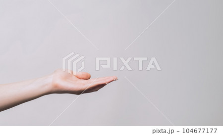 Offering gesture. Open palm. Woman holding copyspace in open hand proposing product isolated on gray empty space background. 104677177