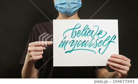 Believe in yourself. Health motivation. Unrecognizable woman in face mask pointing finger at encouraging writing banner on dark free space. Believe in yourself. Health motivation. Unrecognizable woman in face mask pointing finger at encouraging writing banner on dark free space. 104677843