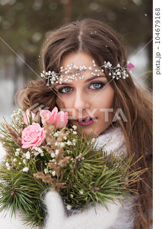 Beautiful bride in a white dress with a bouquet in a snow-covered winter forest. Portrait of the bride in nature. 104679168