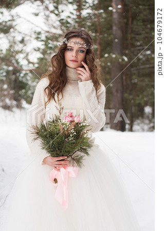 Beautiful bride in a white dress with a bouquet in a snow-covered winter forest. Portrait of the bride in nature. Beautiful bride in a white dress with a bouquet in a snow-covered winter forest. Portrait of the bride in nature. 104679172