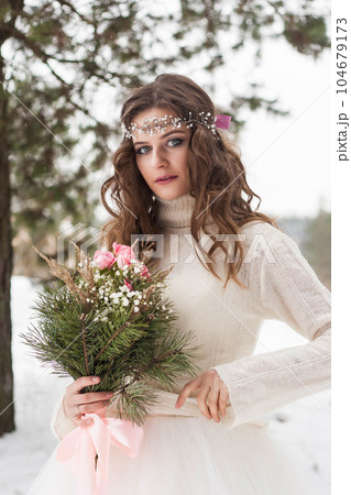 Beautiful bride in a white dress with a bouquet in a snow-covered winter forest. Portrait of the bride in nature. 104679173