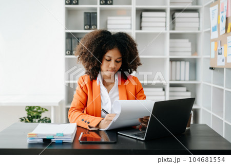 Young African woman typing on tablet and laptop while sitting at the working black table office.. 104681554