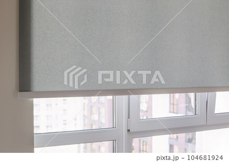Roller blinds automatic close-up on the window. Selective focus. Motorized shades. Gray color curtain, texture fabric. City outside the window. 104681924