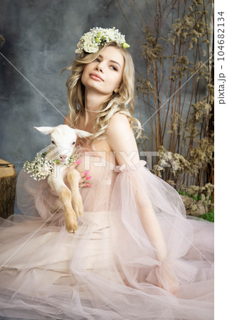 A young blonde woman in an airy pink dress with a white kid. Spring portrait of a woman. A young blonde woman in an airy pink dress with a white kid. Spring portrait of a woman. 104682134
