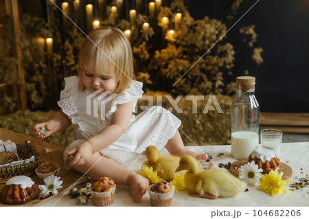A little girl is sitting on the Easter table and playing with cute fluffy ducklings. The concept of celebrating happy Easter. 104682206