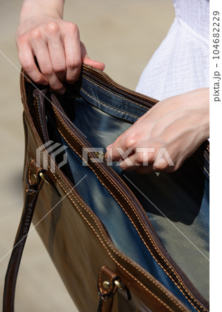 girl in a white summer dress with opened brown handbag posing on the streets 104682229