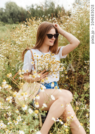 Beautiful young woman in nature with a bouquet of daisies. Field daisies, field of flowers. 104683028