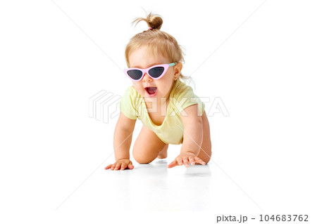 Happy, little girl, toddler in yellow costume and sunglasses crawling on floor and smiling against white studio background 104683762